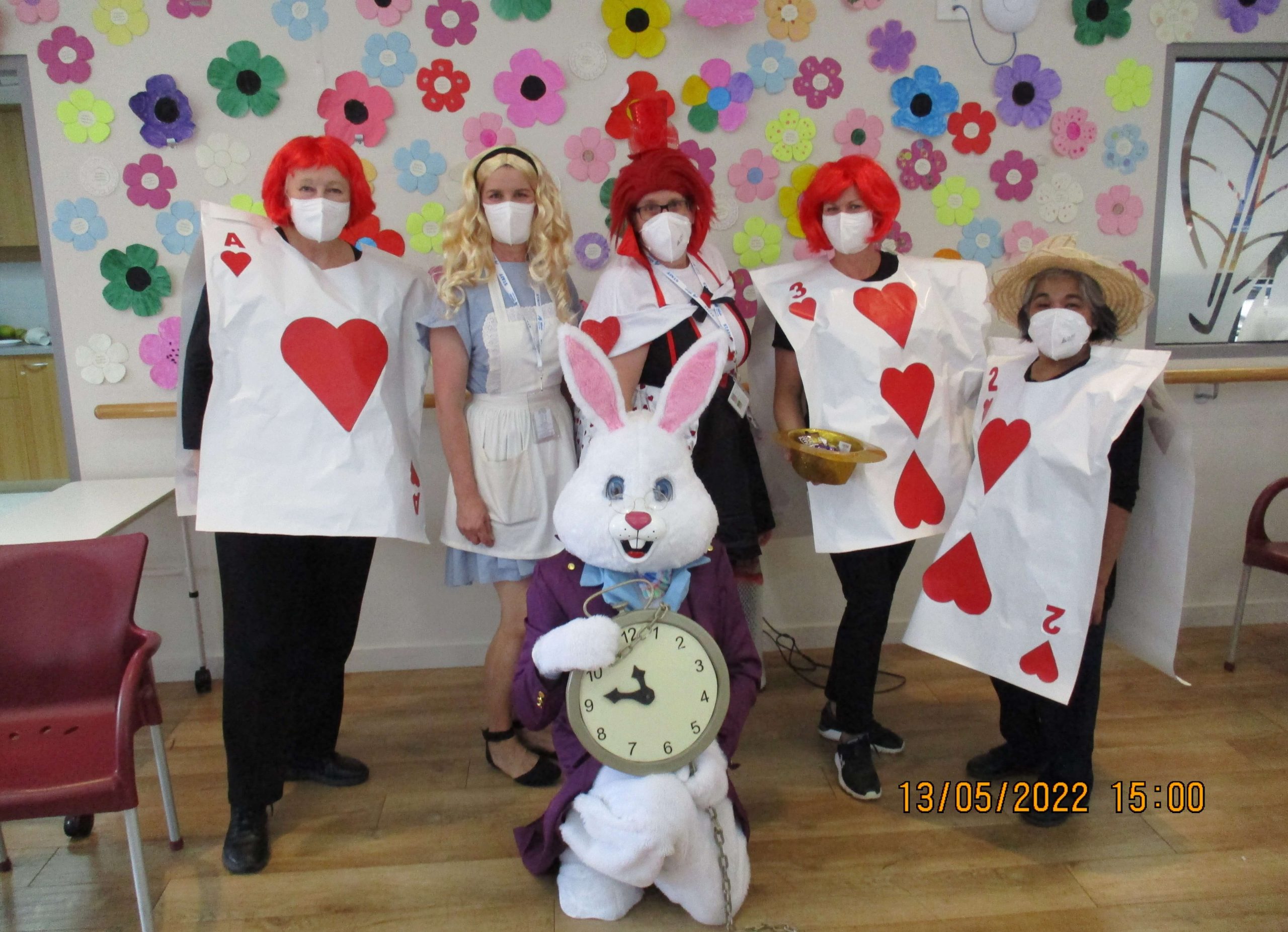 Photo at Yallambee Aged Care with staff dressed up as Alice in Wonderland characters - there is Alice, four 'cards', and a bunny holding a big pocket watch.