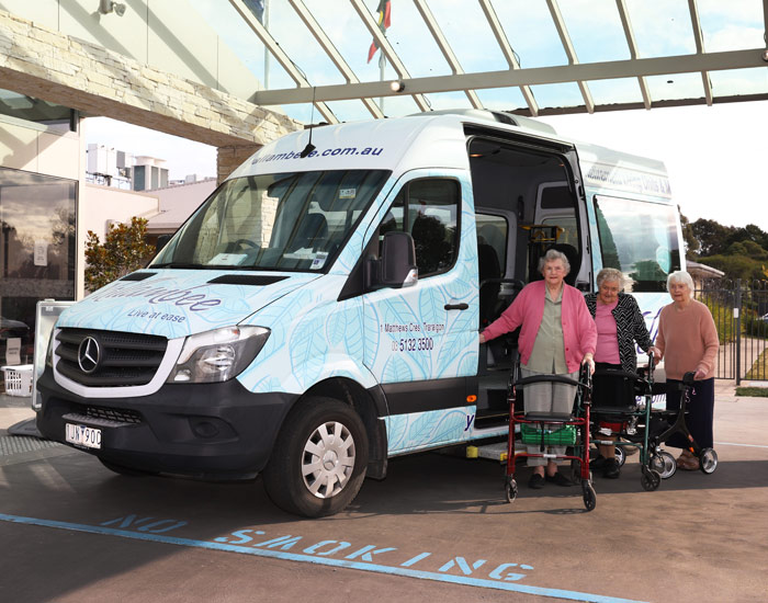 Photo from nursing home of three elderly women with walkers next to a mini bus.
