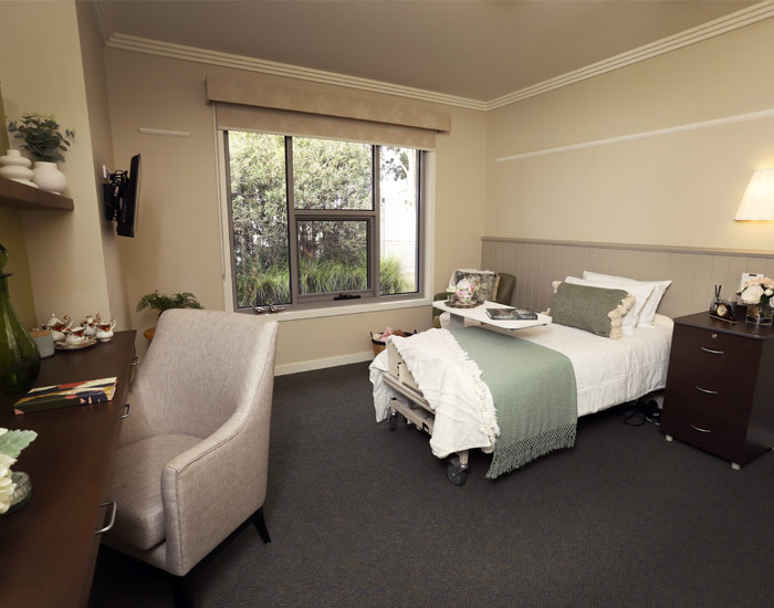 Photo of a lovely bedroom at Yallambee Aged Care, with single bed, armchairs, desk and lots of personal items scattered throughout.
