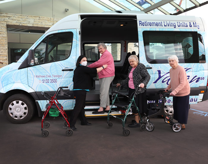 Photo from nursing home of three elderly women with walkers being helped into a bus by a younger woman.