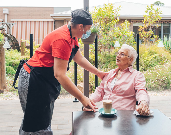 Photo an outdoor garden areas and cafe staff member giving a coffee latte to elderly women who is sitting down.